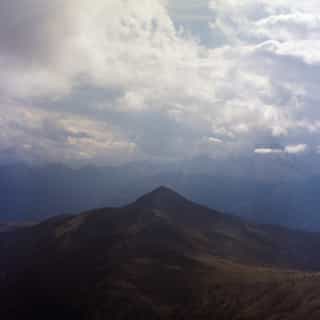 Dark mountain ridge rising before distant hazy peaks and a clouded sky