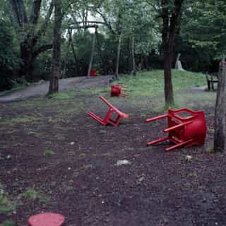 Bright red chairs overturned and scattered across a dirt clearing in a wooded park